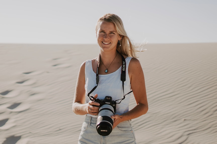A female photographer stands on a beach smiling