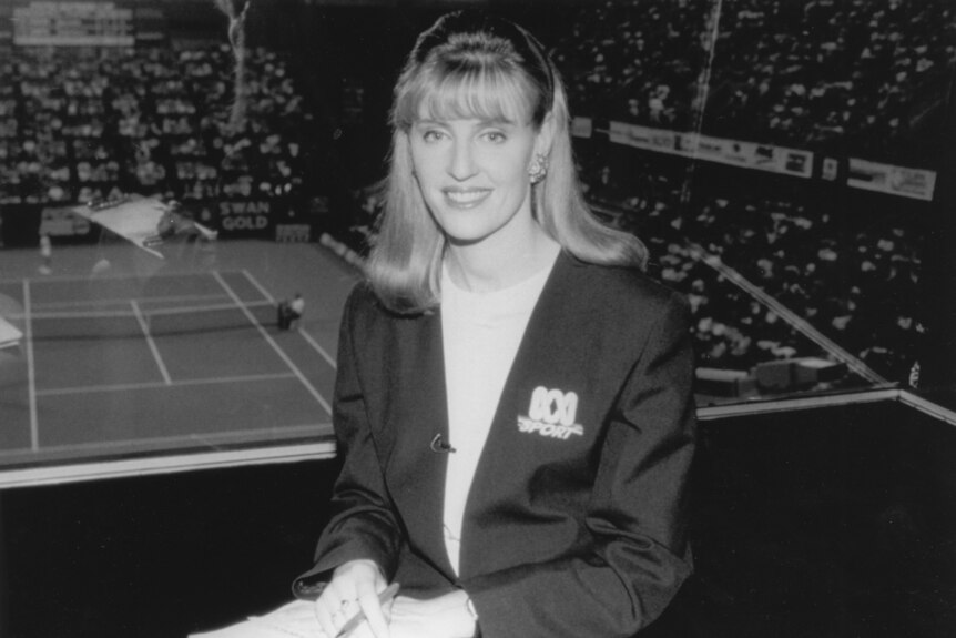Black and white photo of Tighe in broadcast box with tennis court in background.