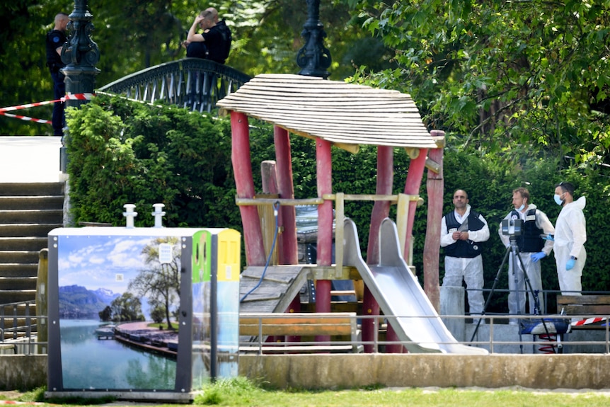 Three men in forensic gear gather at playground.