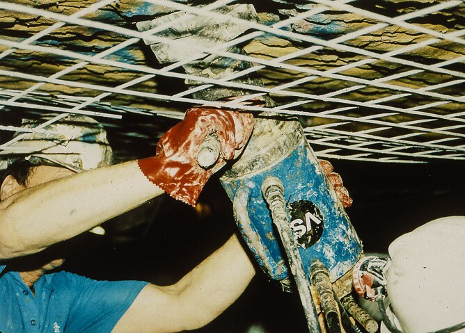 A man  holds a piece of construction machinery up against a rock ceiling