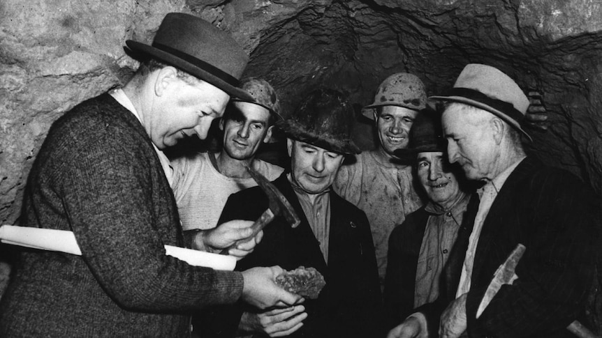 B&W photo of five men in a mine - one with a piece of yellowcake in his hand showing it to others