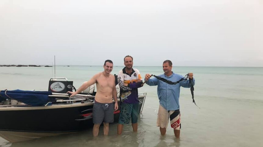 Fishermen Julio Fraccaro, Ben Pearce and Kim Ford hold up the burnt fishing rod from a lightning strike
