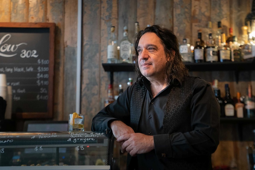 A black haired man looks left against a bar