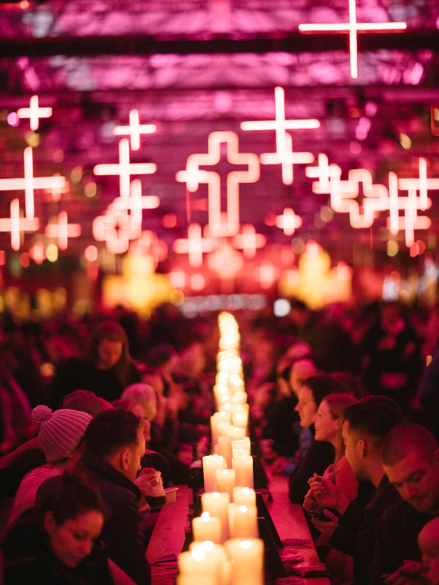 People seated at a long table with illuminated crosses overhead.