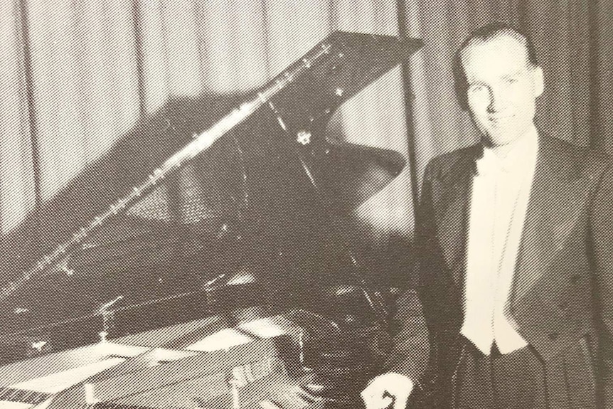Younger Albert Fox dressed in a suite stands next to a piano