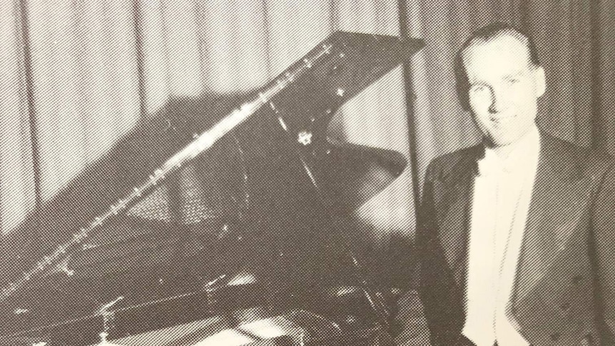 A man dressed in a suit stands next to a piano.