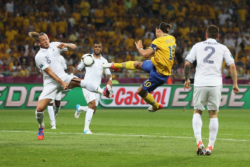 A Swedish soccer striker hits a right-foot volley from mid-air as he is surrounded by French defenders.