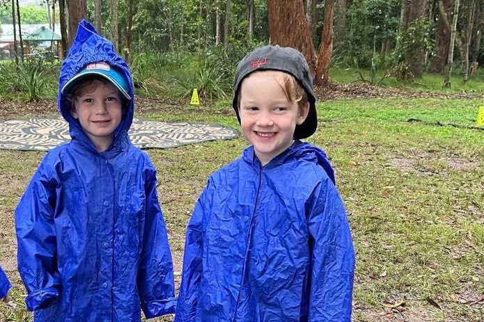Two kids in raincoats in the bush.