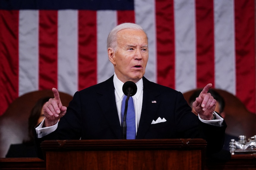 Joe Biden, suit with blue tie, using both hands to point to a crowd while speaking.