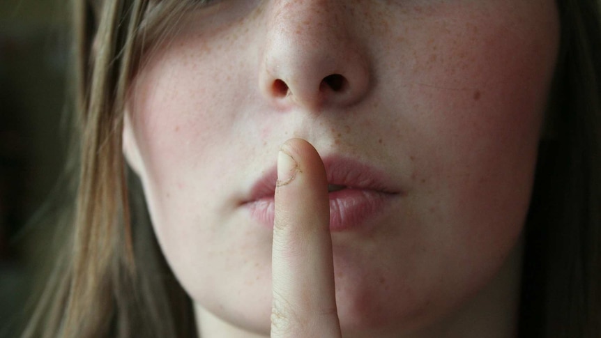 s woman holds her finger to her lips giving the sign for silence