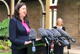 Annastacia Palaszczuk speaks at a podium surrounded by microphones and the Chief Health Officer Jeannette Young watches on