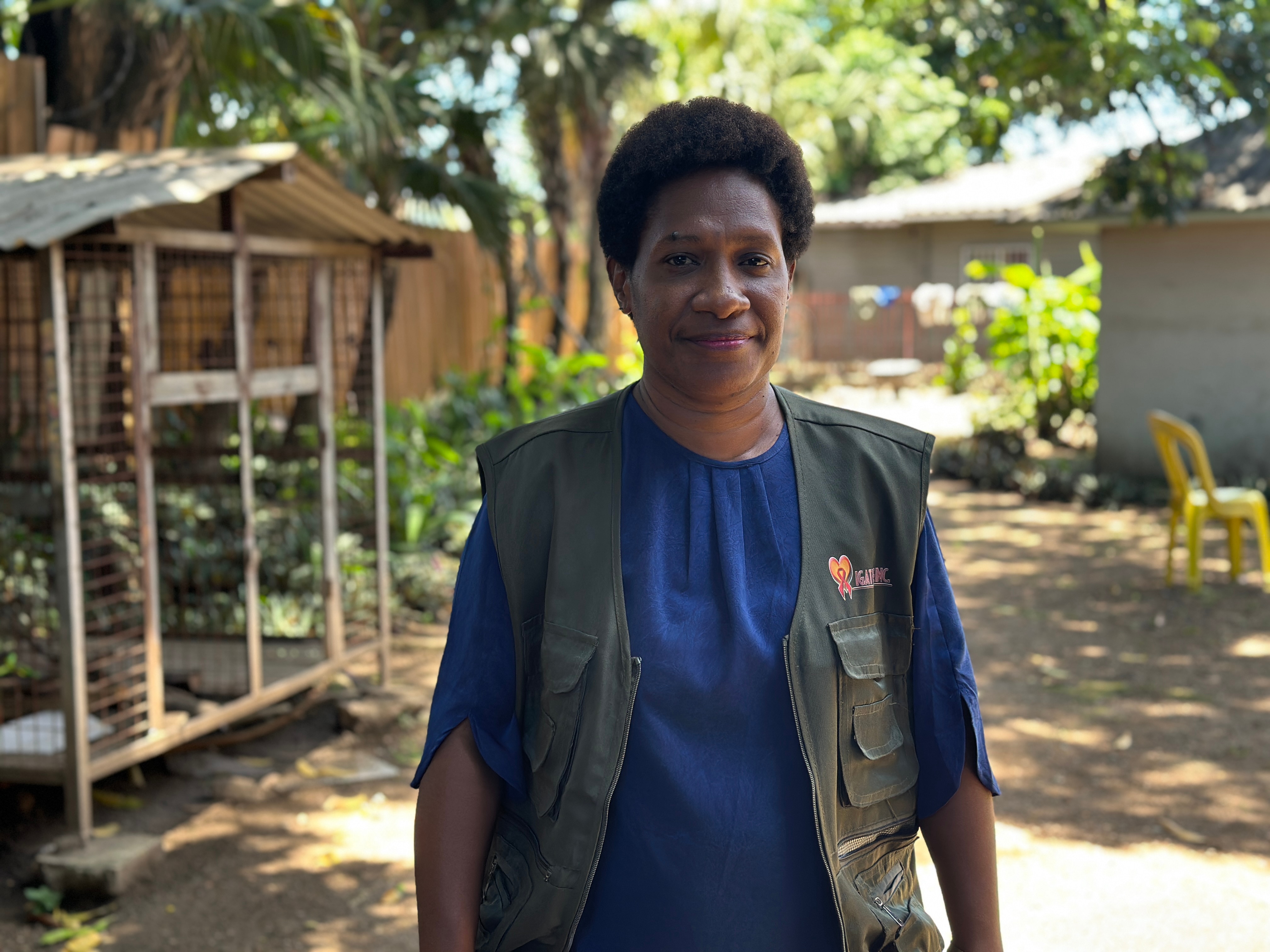 Una mujer sonríe a la cámara con un chaleco verde y una camisa azul.