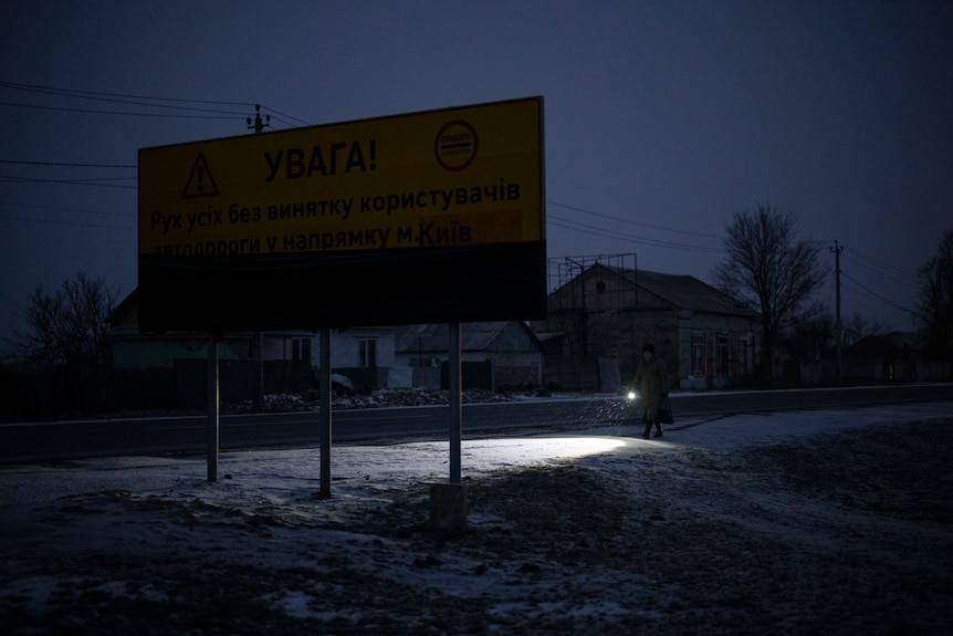 A torch shines along a dark road with a large sign. 