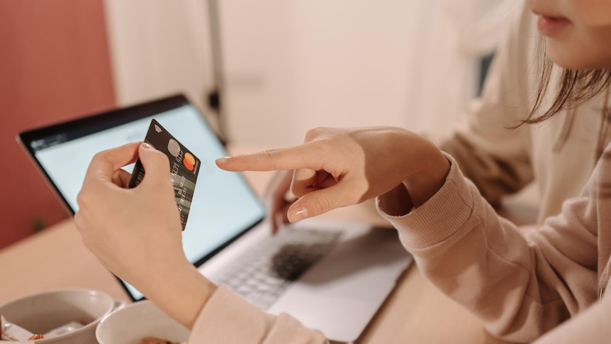Woman's hand holds a credit card in front of a computer 