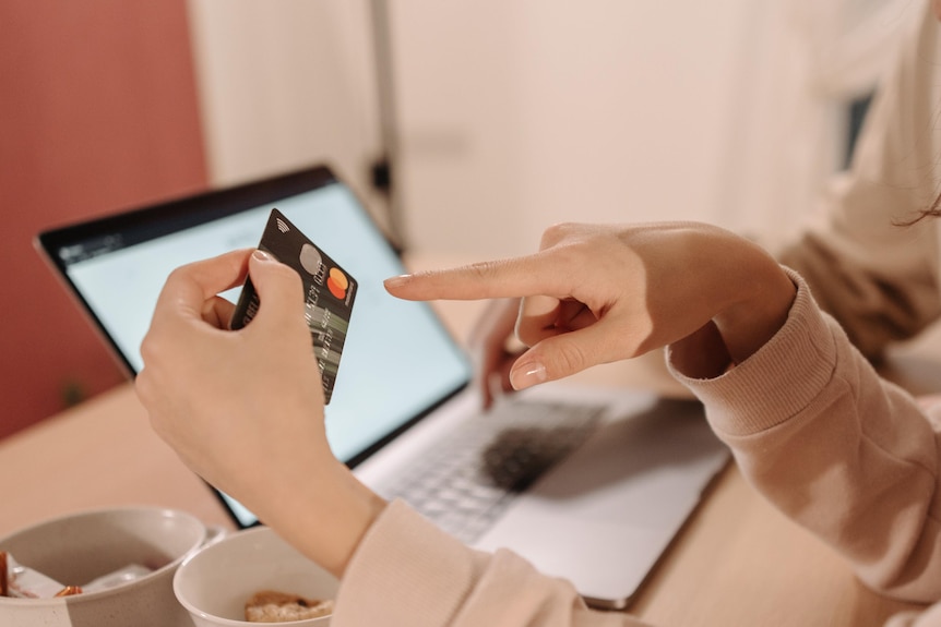 La mano de una mujer sostiene una tarjeta de crédito frente a una computadora 