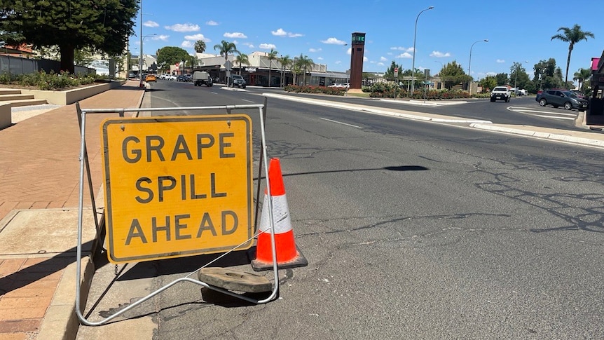 A bright yellow sign on a road that says grape spill ahead