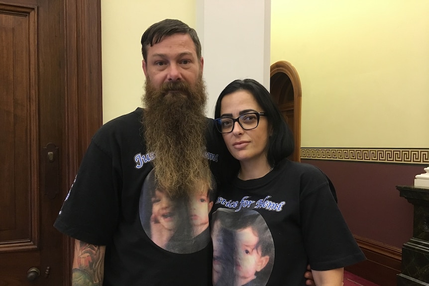 Hemi's parents, wearing shirts with his photo, stand in Queensland's Parliament House.