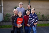 On an overcast day, you view a Chinese-Australian family staring into the camera while standing in their backyard.