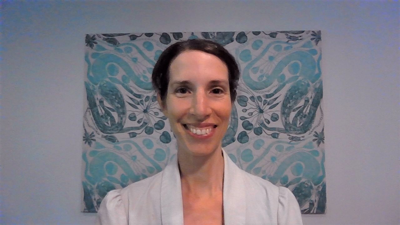 A lady with dark hair stands in front of blue artwork