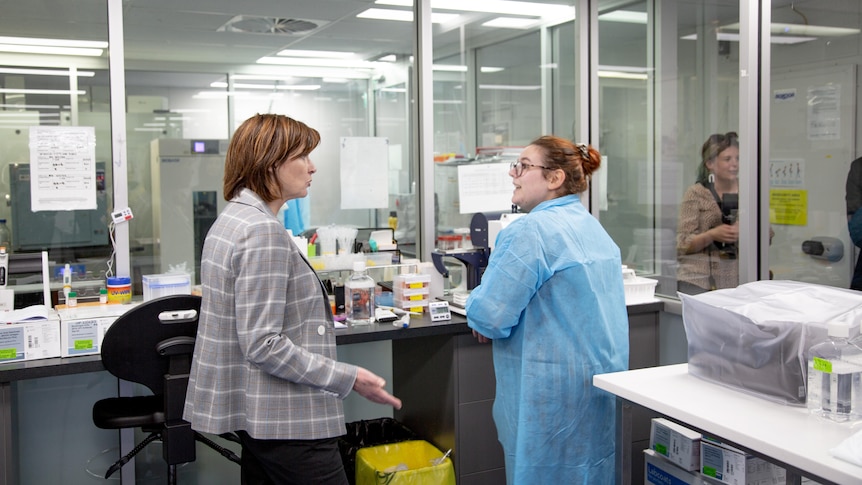 Woman talking to another woman in a blue lab coat in a lab