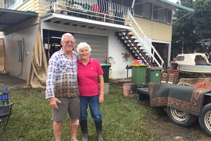 A couple stands together outside their flooded home in Lismore.