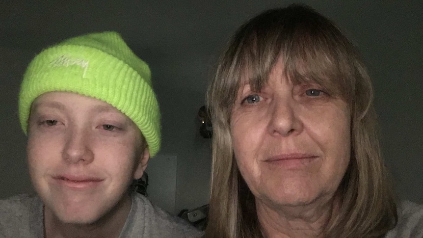 A 16-year-old boy with cancer wears a beanie with his mother