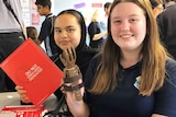 Two Year 8 students hold up a finished prosthetic hand in a classroom at school.
