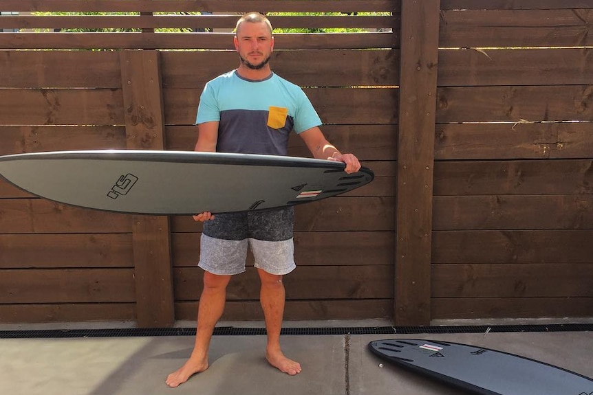 Man holding a surfboard, with two other surfboards near his feet