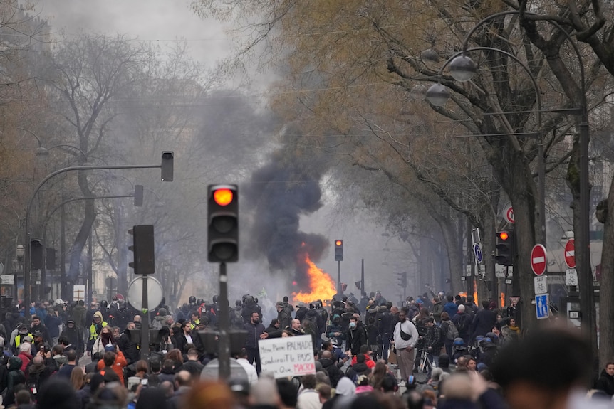 a crowd of people crowd the streets in Paris as a fire burns in the background