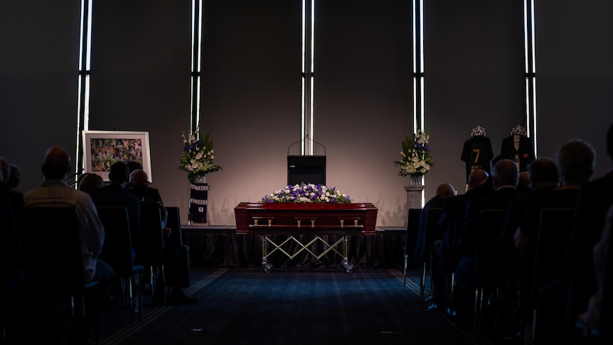A casket with flowers in front of a stage