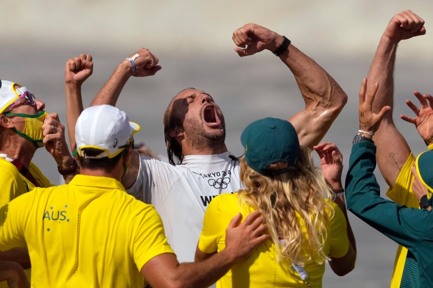 Owen Wright shouts with his fists pumped, while surrounded by his support team wearing green and gold.