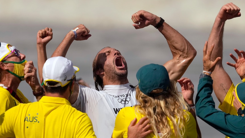 Owen Wright shouts with his fists pumped, while surrounded by his support team wearing green and gold.