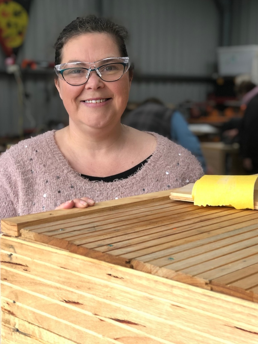 Woman wearing safety goggles standing behind a woodwork project