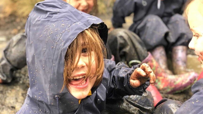 A smiling child plays in a "mud pit" with others at school.