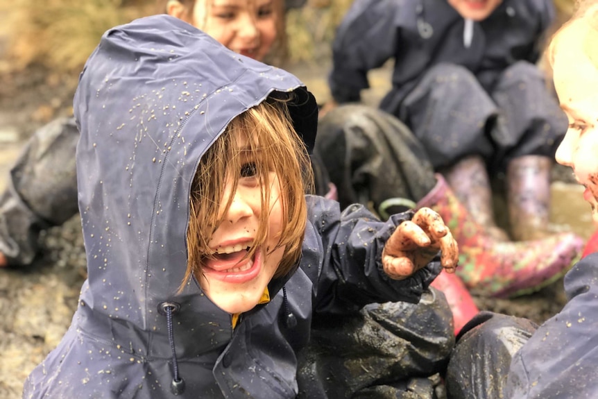 A smiling child plays in a "mud pit" with others at school.