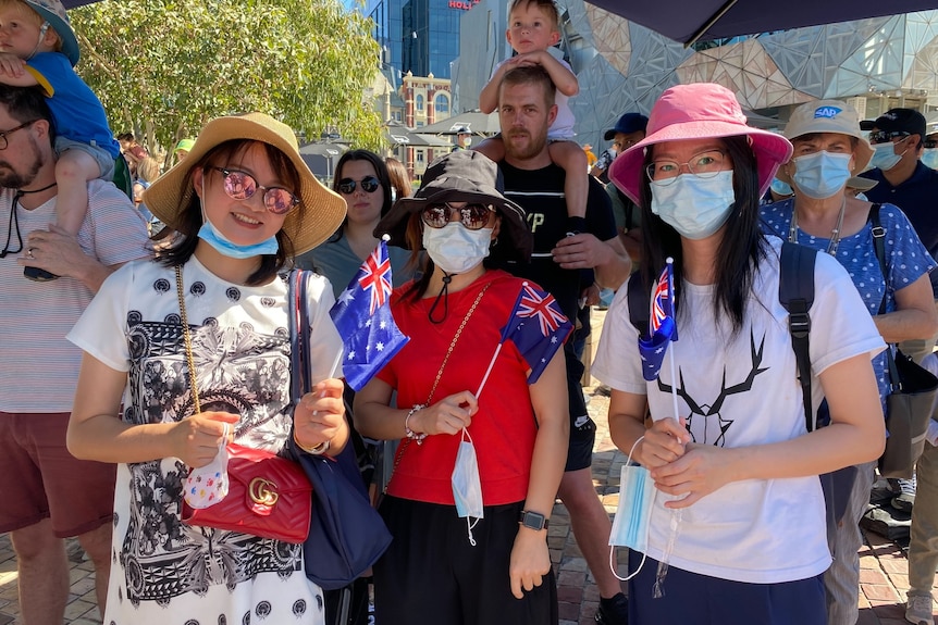 A group of people, many wearing face masks and waving Australian flags at Federation Square.