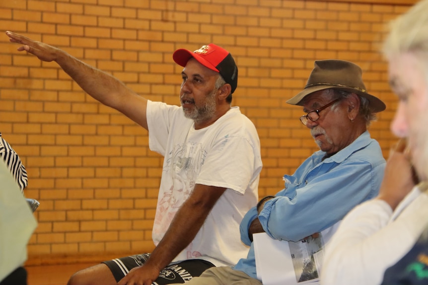 Two Aboriginal men sitting in a chair. One is holding his hand out and talking.