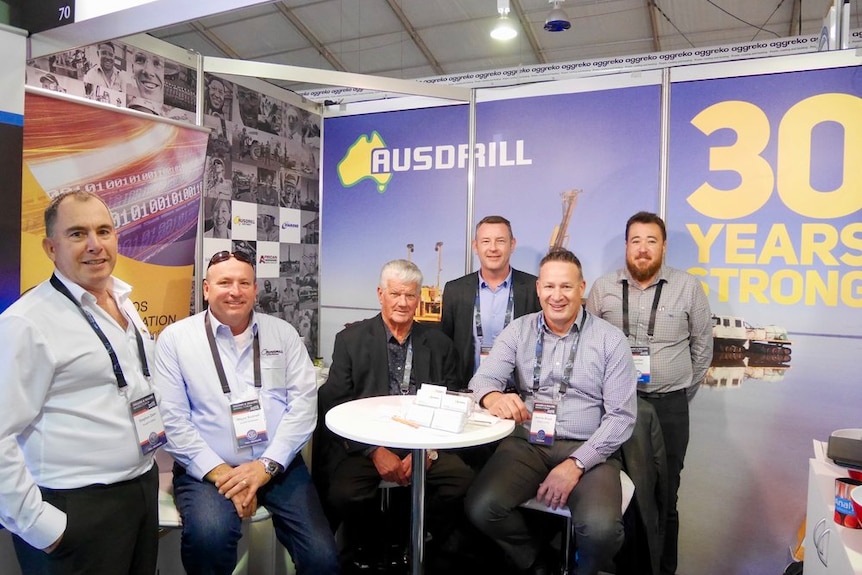 A group of men in a booth at a mining convention.  