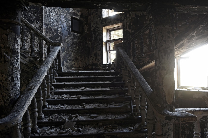 An ornate interior staircase and the walls around it are burned black, the stairs littered with debris