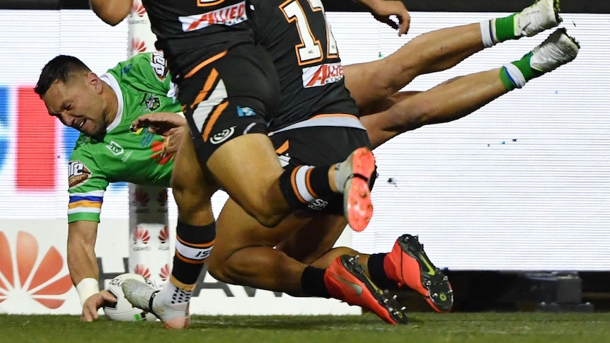 An NRL player reaches out mid-air to plant the ball down in the corner for a try.