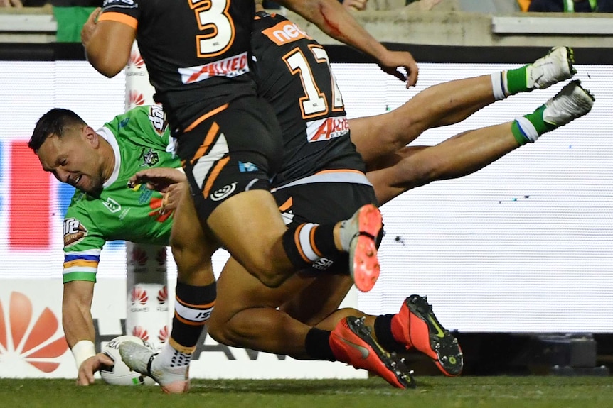 An NRL player reaches out mid-air to plant the ball down in the corner for a try.