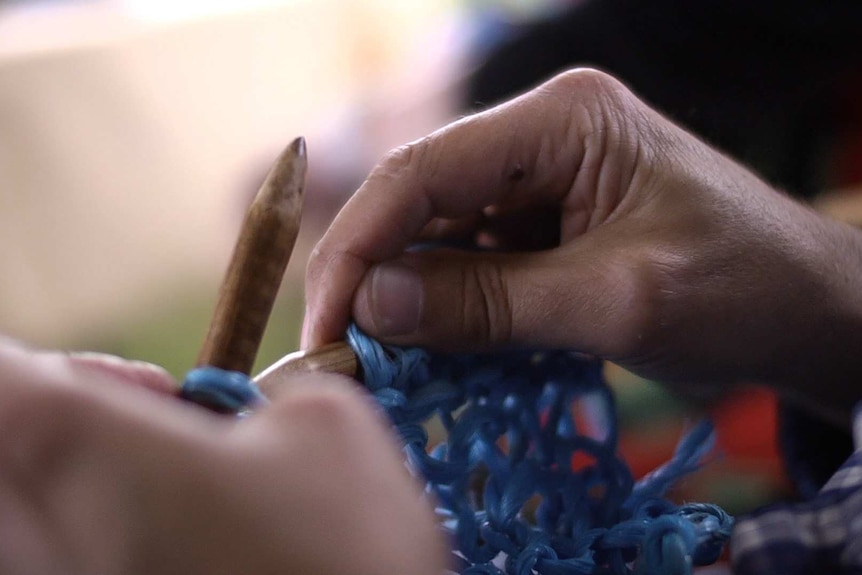 Close up of hands knitting with giant needles and baling twine