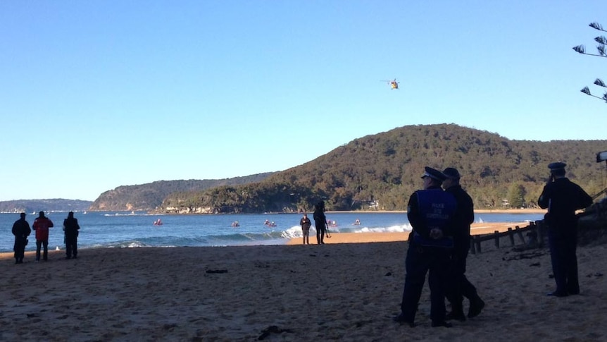 Police stand on the beach as boats search the waters off Pearl Beach.