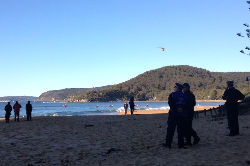 Police stand on the beach as boats search the waters off Pearl Beach.