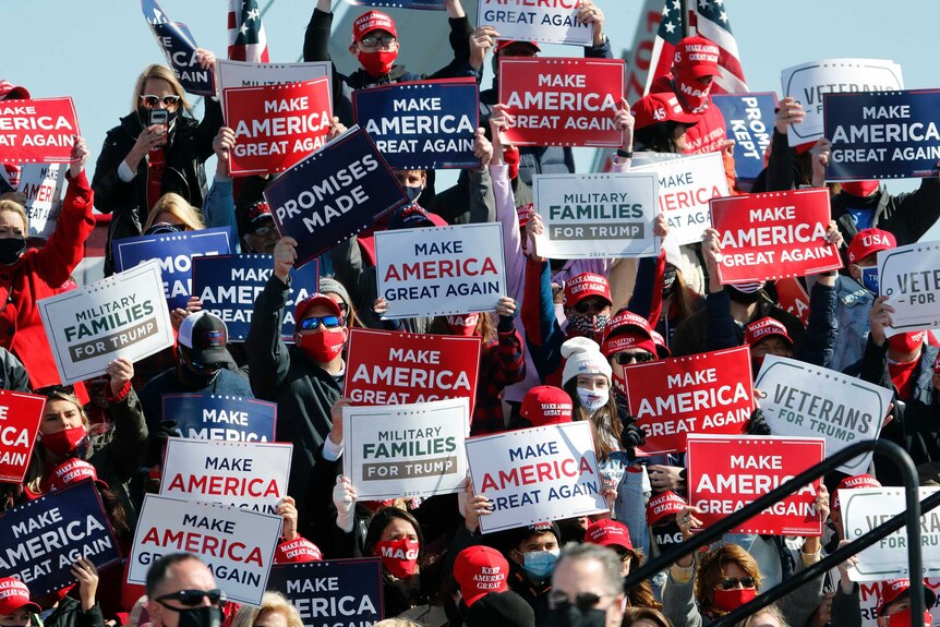A crowd of people wearing masks and caps hold up MAKE AMERICA GREAT AGAIN signs