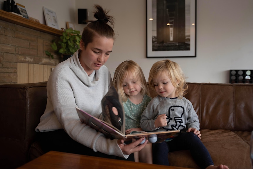 A woman and two children reading a book.