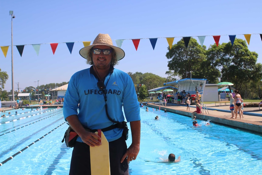 Lifeguard Nathan Hall stands in front of the busy Speers Point Pool during the heatwave.