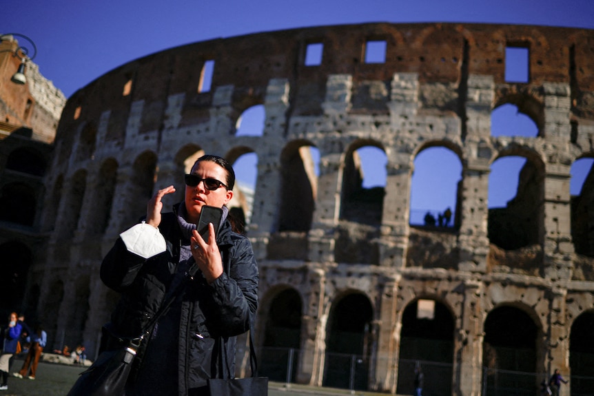 A woman talks on the phone as she holds a mask in her hands outside Rome's Colosseum