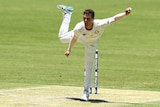 A spin bowler lands on one leg post delivery, with his arms outstretched and his other leg in the air behind him.