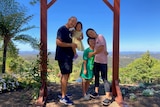 A mum and dad with their two kids stand in front of an archway with blue sky and mountains behind 
